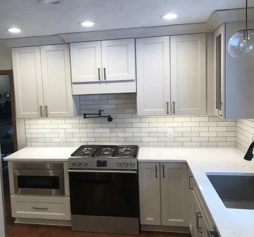 White cabinets, subway tile backsplash, range, and sink in a compact kitchen.