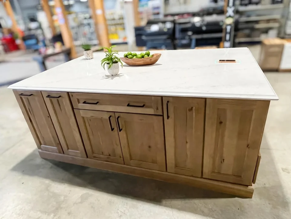 Wood kitchen island with paneled cabinet doors, dark handles, and a pale countertop in a workshop.
