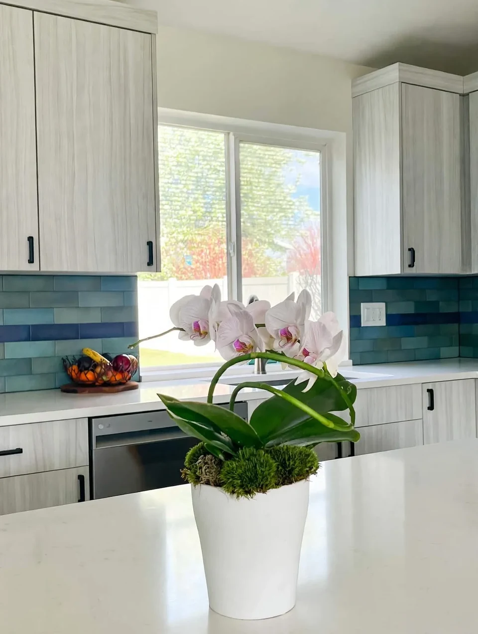 White kitchen cabinetry, a window, and an island sink with flowers.