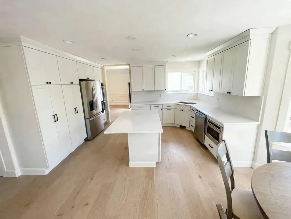 Wide view of a pale kitchen with a white island and dark refrigerator.