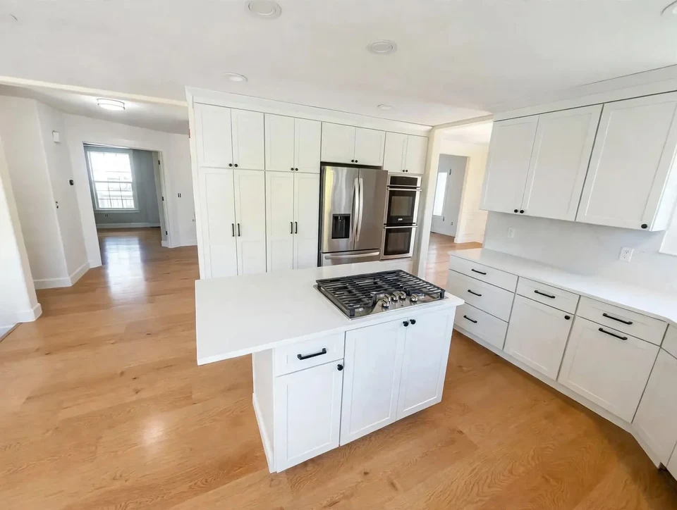 Kitchen with a white island, white cabinets, and light wood flooring.
