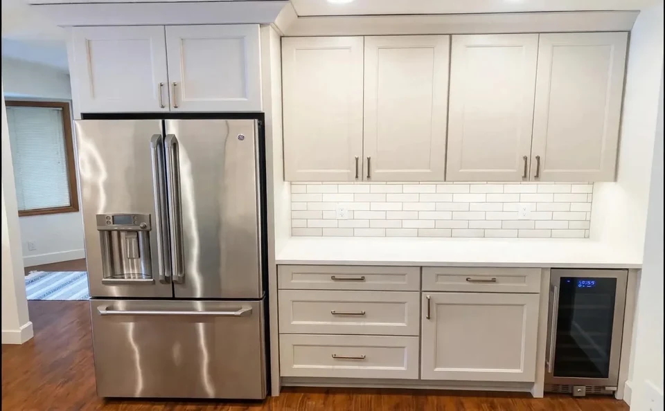 White kitchen cabinets framing a stainless steel refrigerator and under-counter beverage cooler.