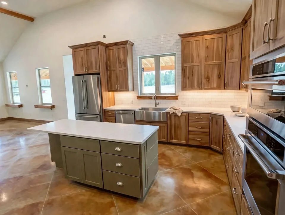 Natural wood kitchen cabinetry around a window with a central island and pale countertops.