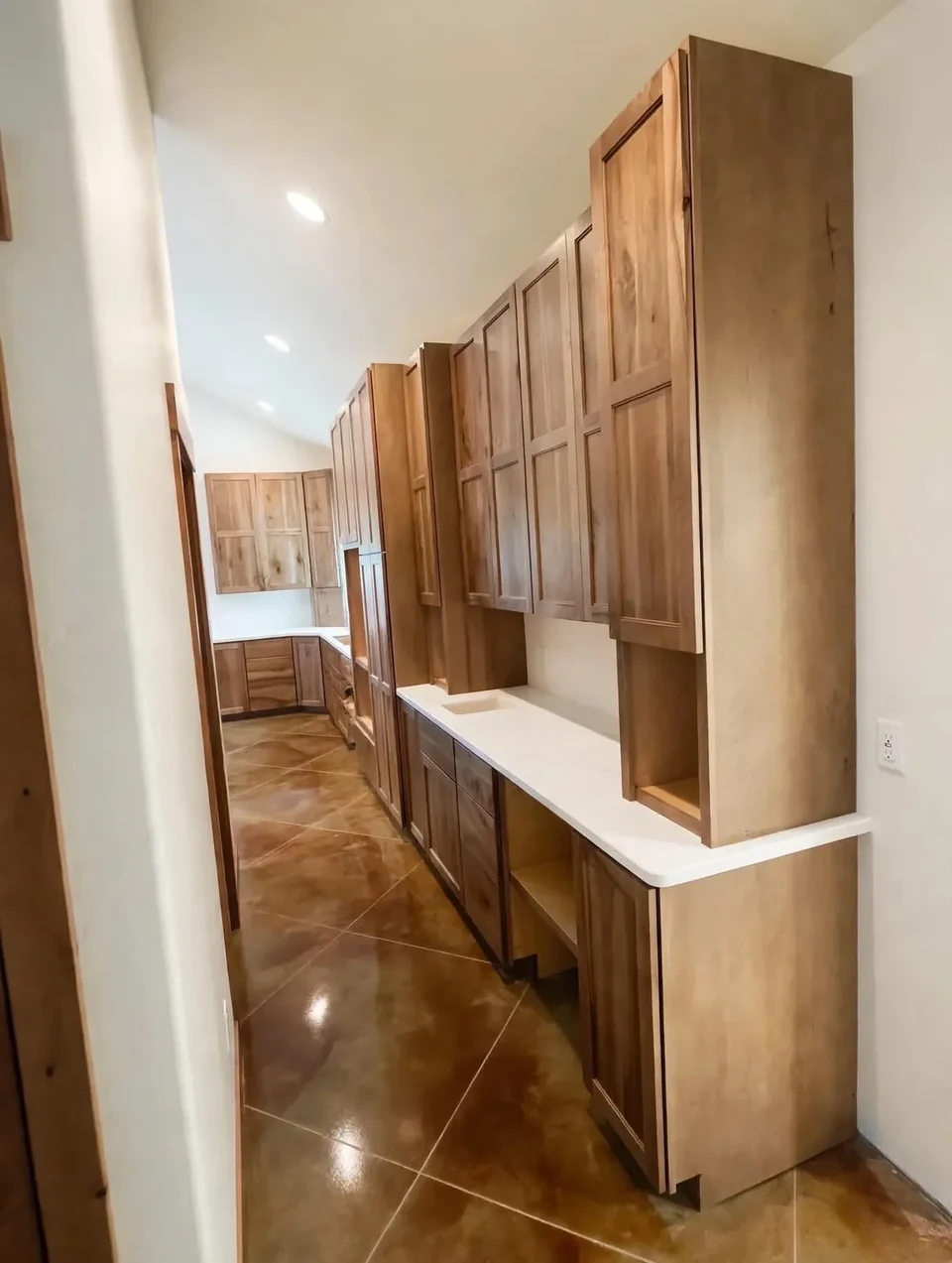 View along a kitchen with natural wood cabinets, pale counters, and wood flooring.