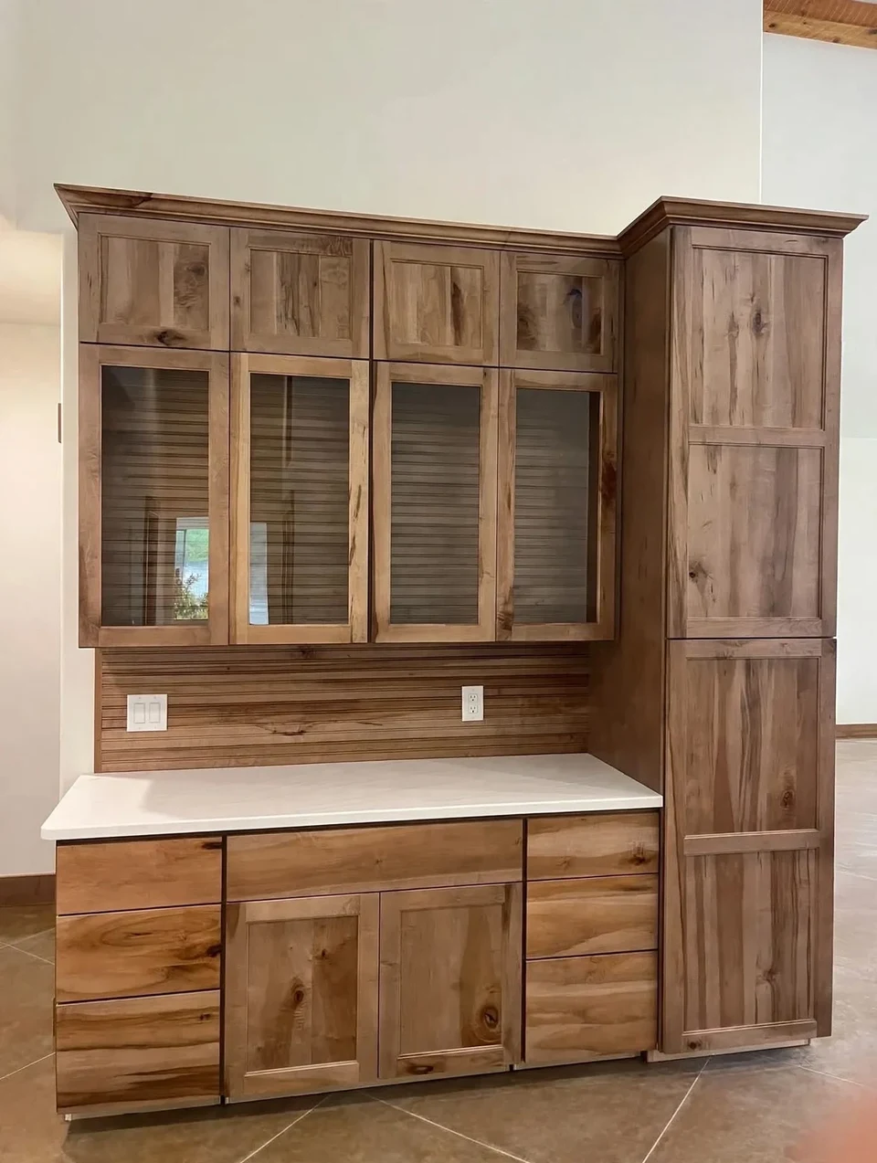 Natural wood built-in cabinetry with glass-front upper doors, a pale countertop, and tall cabinet storage.