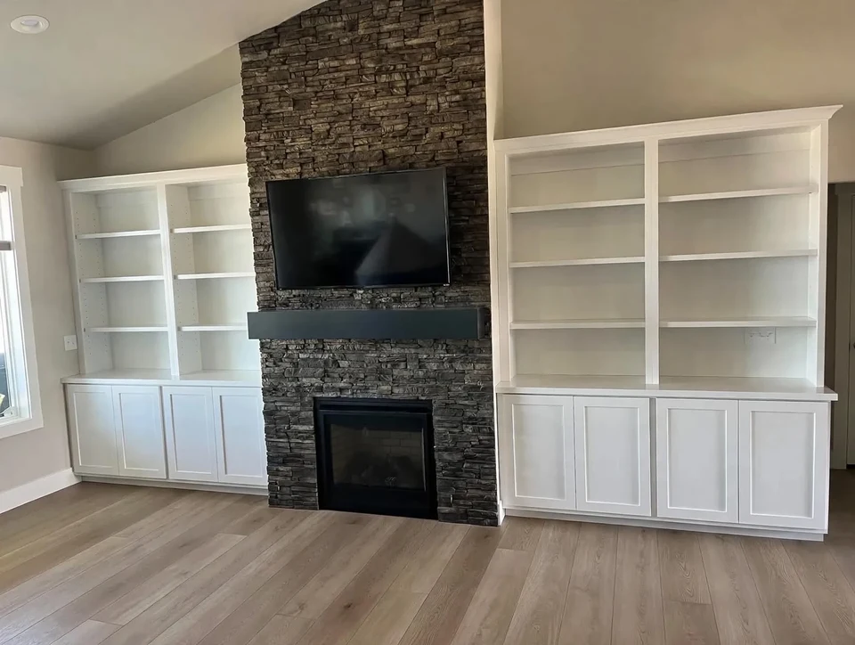 White built-in shelves and cabinets on both sides of a dark stone fireplace with a wall-mounted television.