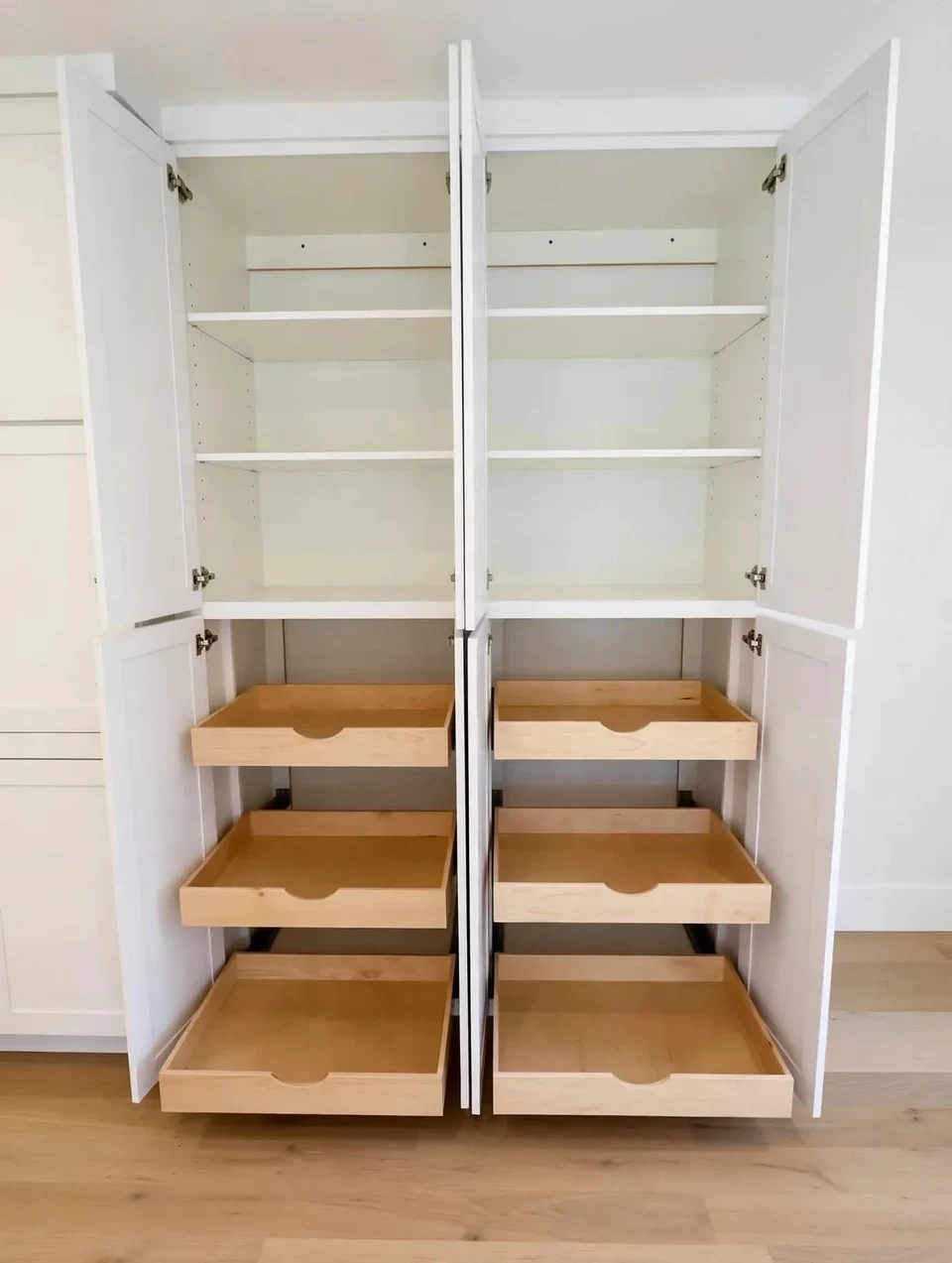 Open white pantry cabinet with adjustable shelving above three natural wood pull-out drawers.