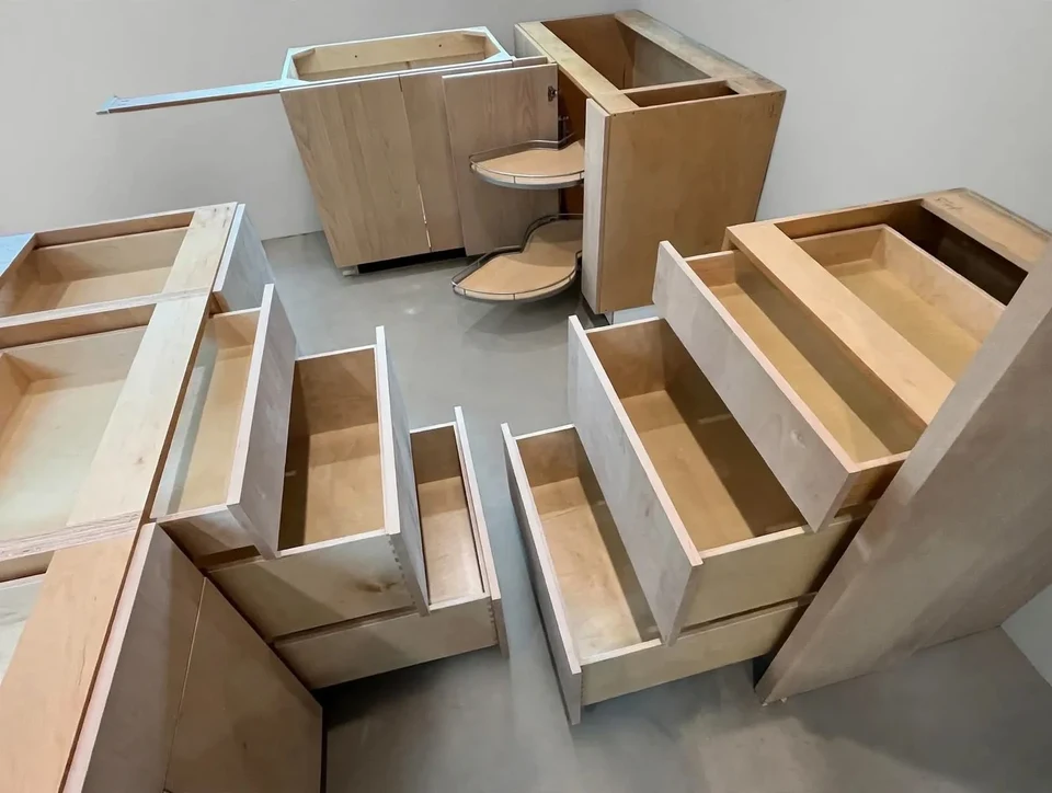 Unfinished wood cabinet boxes and drawers arranged on a concrete workshop floor.
