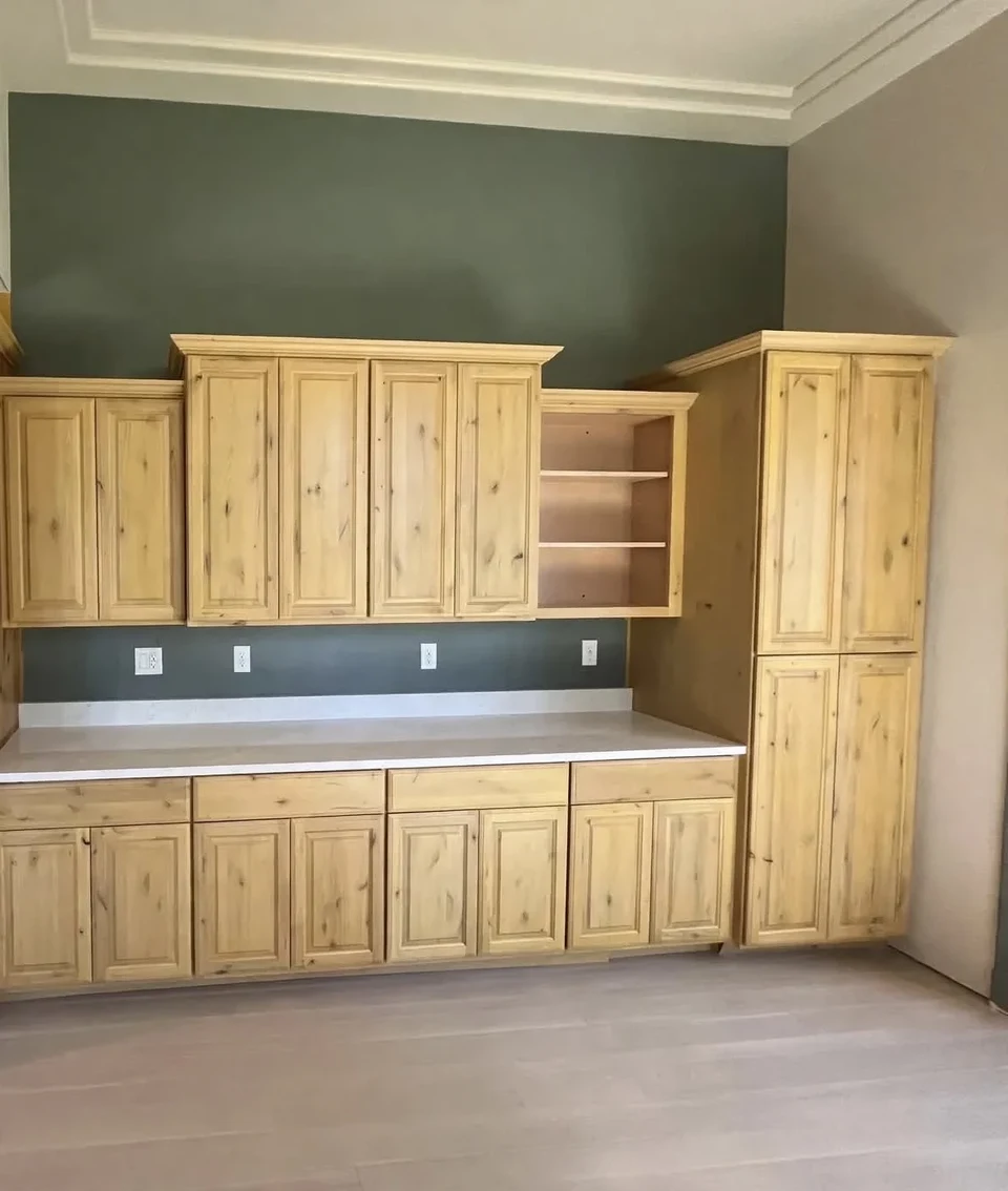 Natural wood built-in cabinetry with tall upper cupboards, central open shelving, and a dark countertop against a green wall.